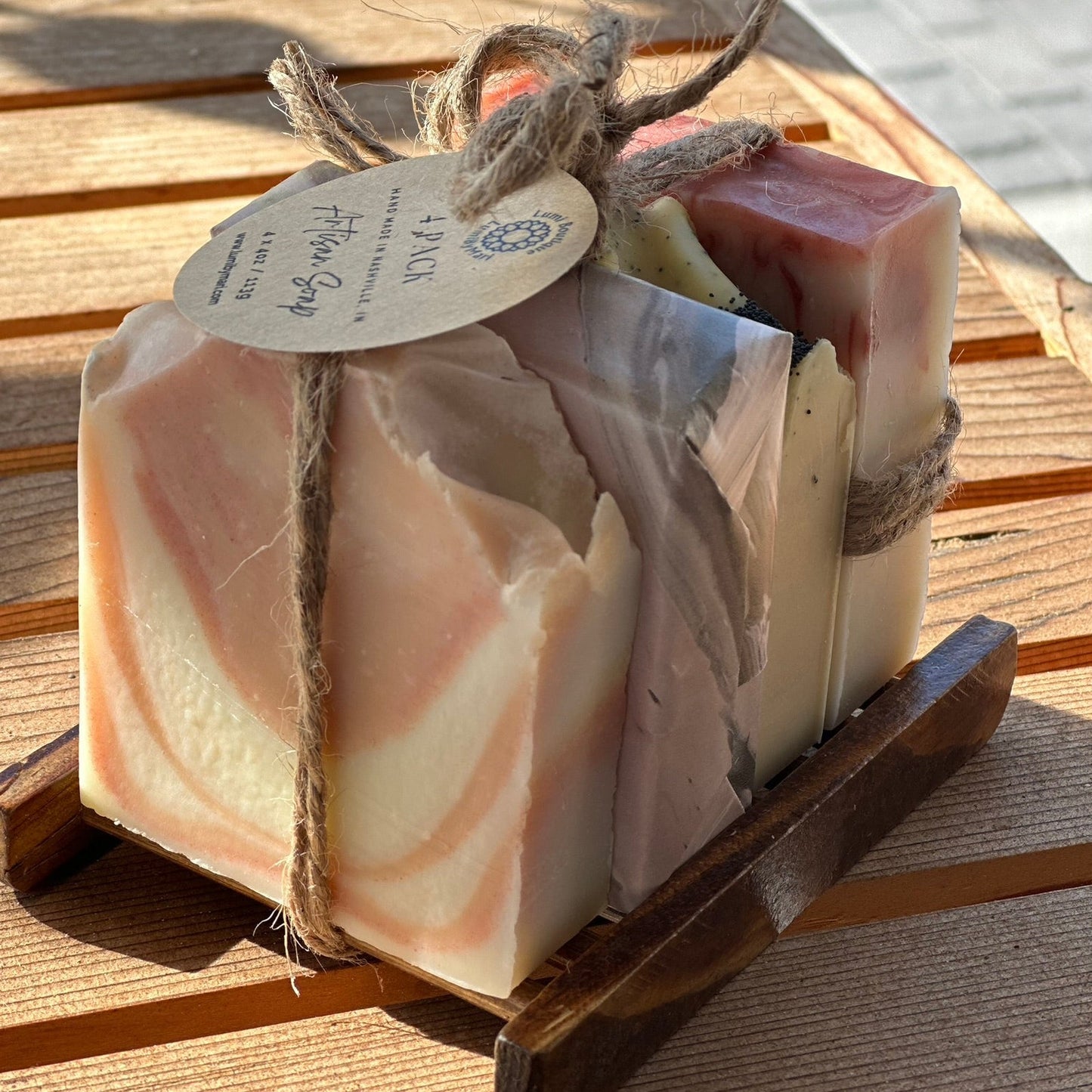Small set of soap bars in a wooden holder with a visible brand tag on a wooden surface.