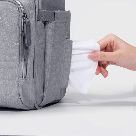 Gray backpack with a hand pulling out a white paper towel from a dispenser attached to the backpack.