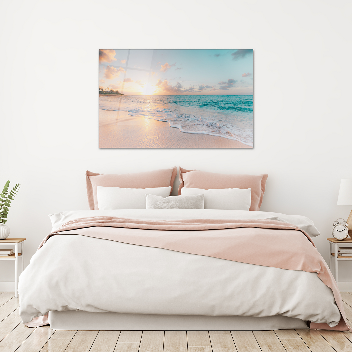 A canvas wall art print depicting a beach scene with the sun setting over the ocean, displayed above a bed in a room with wood floors