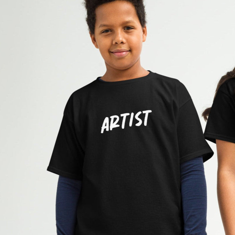 Two children, one male and one female, wearing black crew neck t-shirts with the word 'ARTIST' printed on the front, standing against a neutral background.