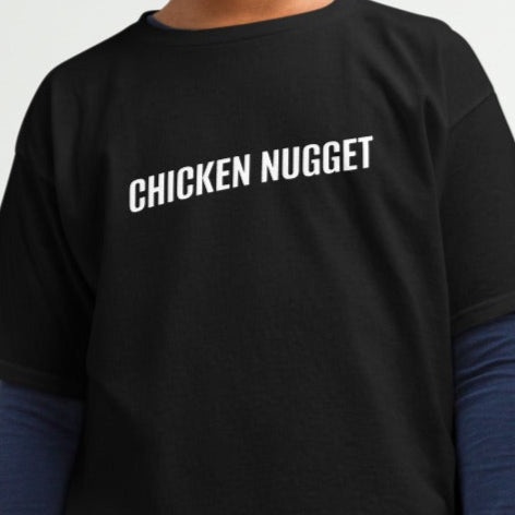 Youth wearing black T-shirt with the text 'CHICKEN NUGGET' standing against a neutral background.