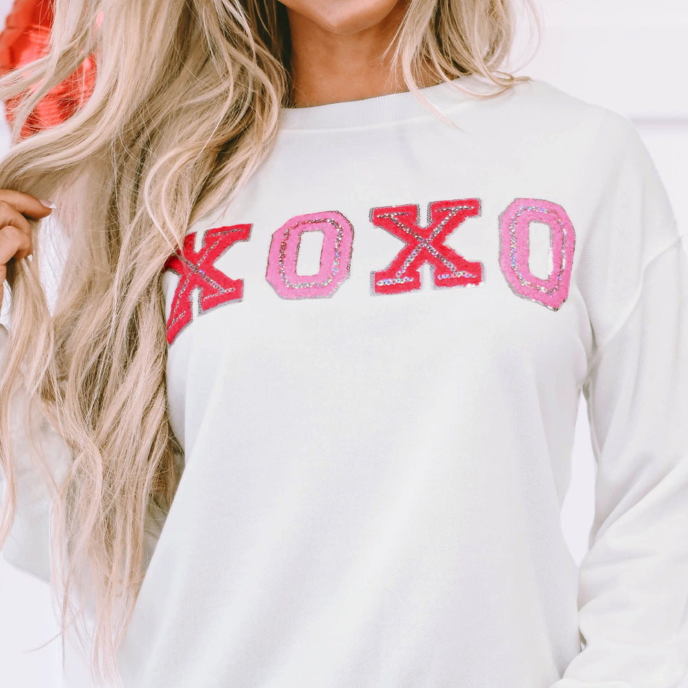 Person wearing a white sweatshirt with 'XOXO' in red and pink letters.