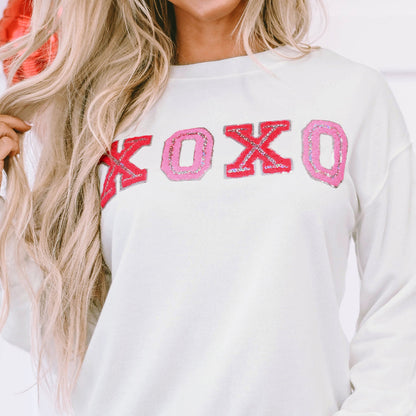 Person wearing a white sweatshirt with 'XOXO' in red and pink letters.