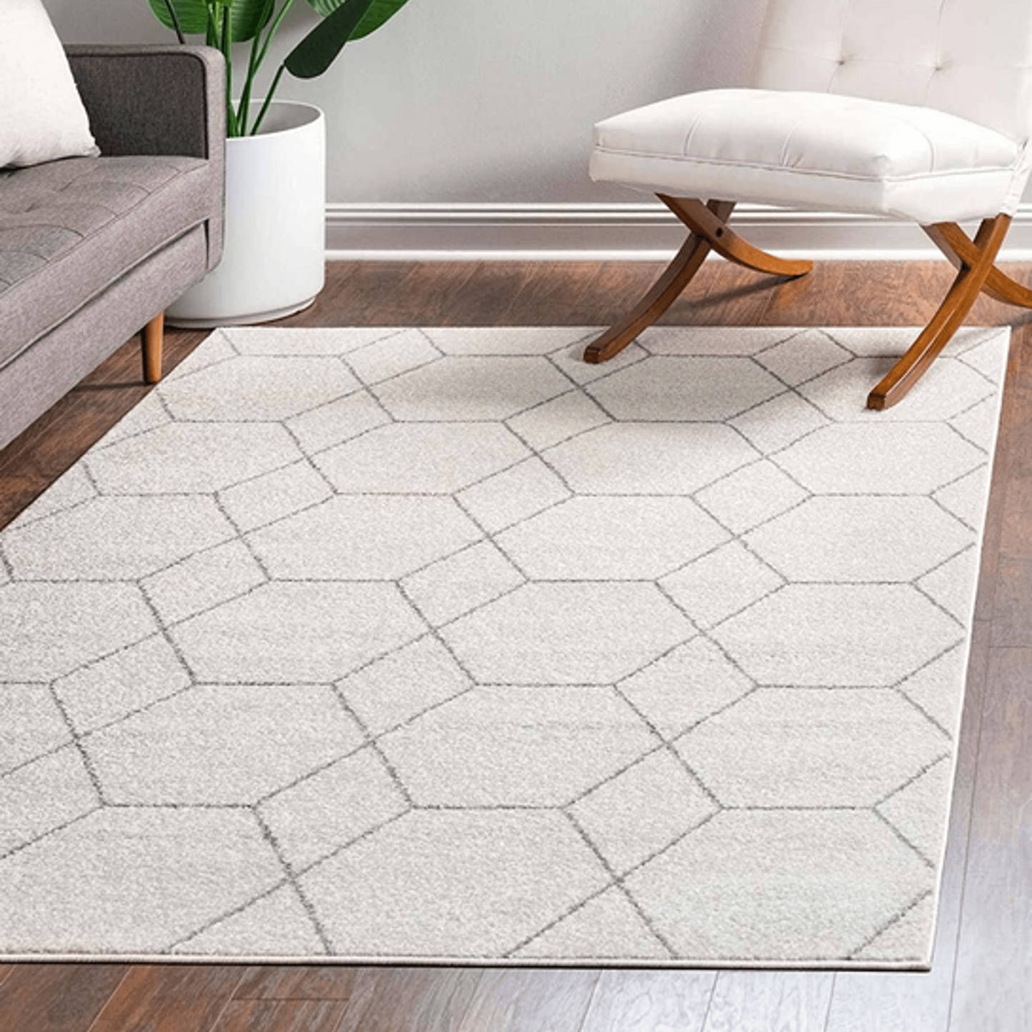 Living room with a geometric patterned rug, gray sofa, white chair, and plant.
