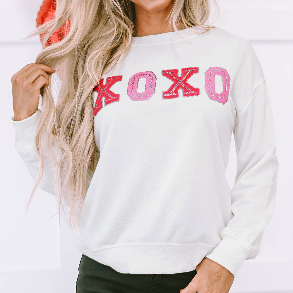 Woman wearing a white sweatshirt with 'XOXO' in pink letters, standing against a white background.