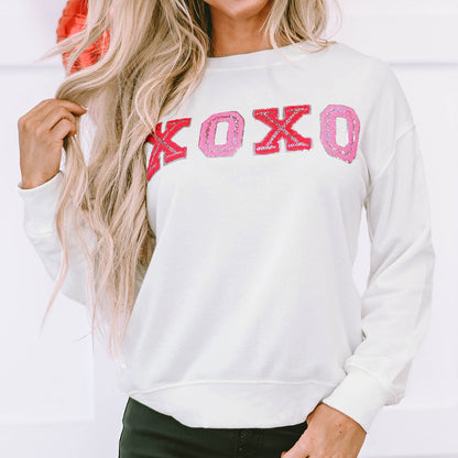 Woman wearing a white sweatshirt with 'XOXO' in pink letters, standing against a white background.