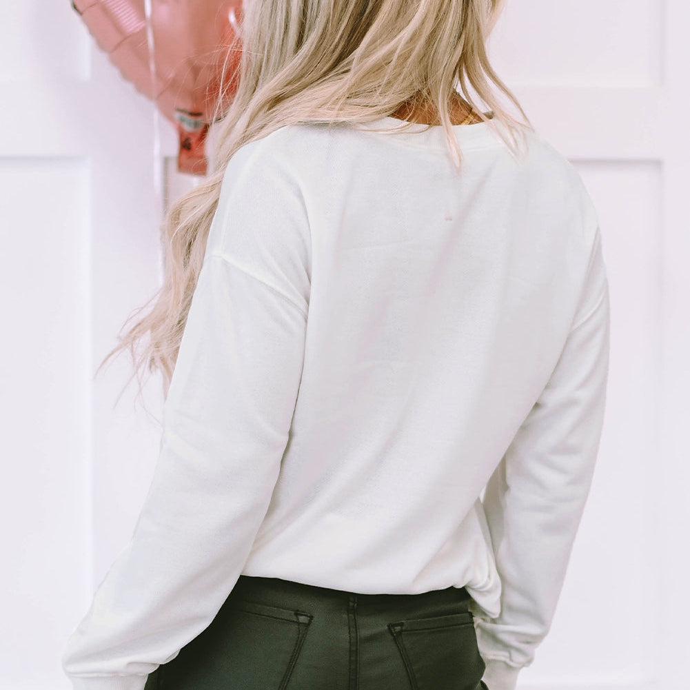 Person wearing a white long-sleeve top and dark pants with heart-shaped balloons in the background.