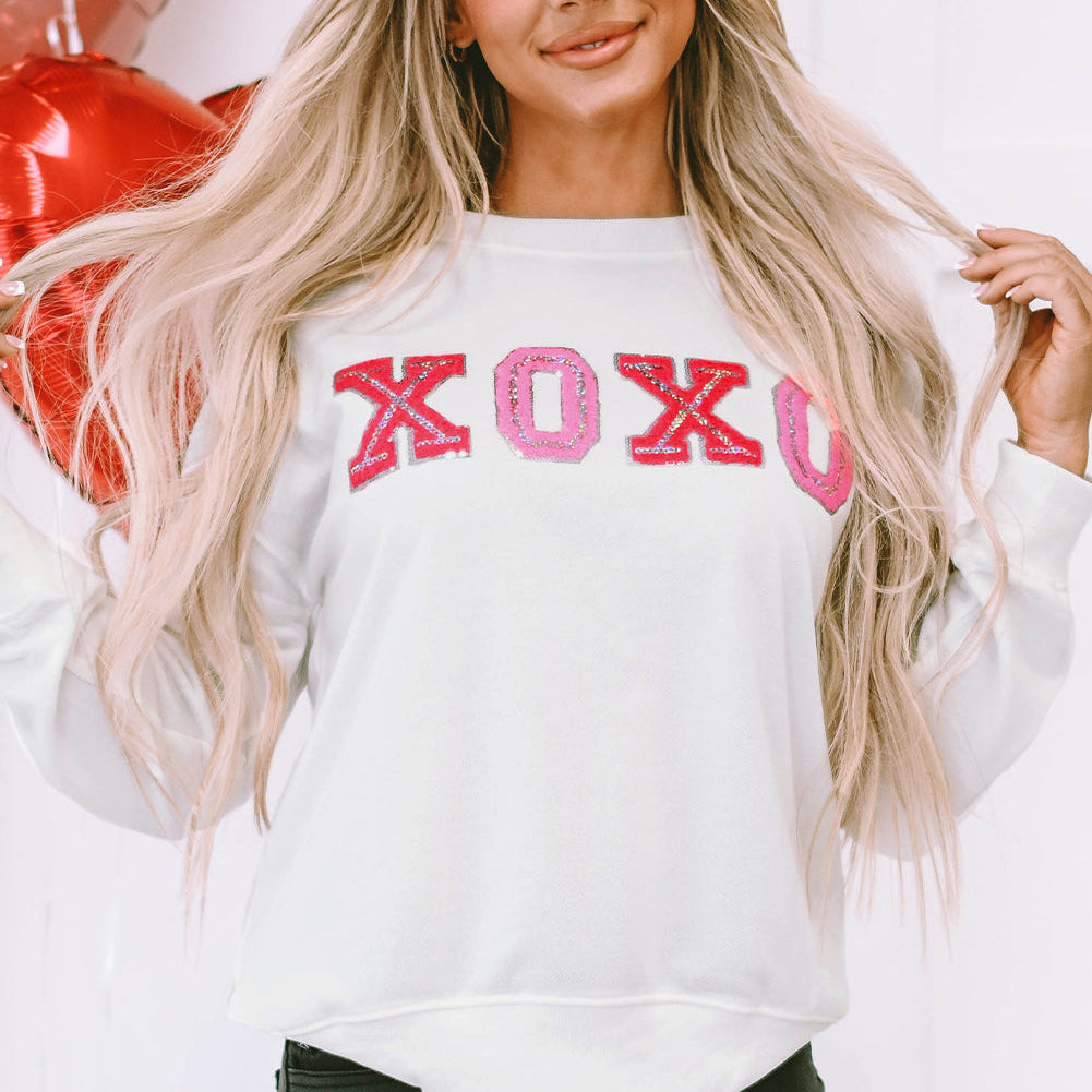 Woman wearing a white sweatshirt with 'XOXO' in pink letters, standing against a white background.