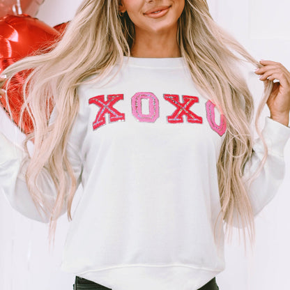Woman wearing a white sweatshirt with 'XOXO' in pink letters, standing against a white background.