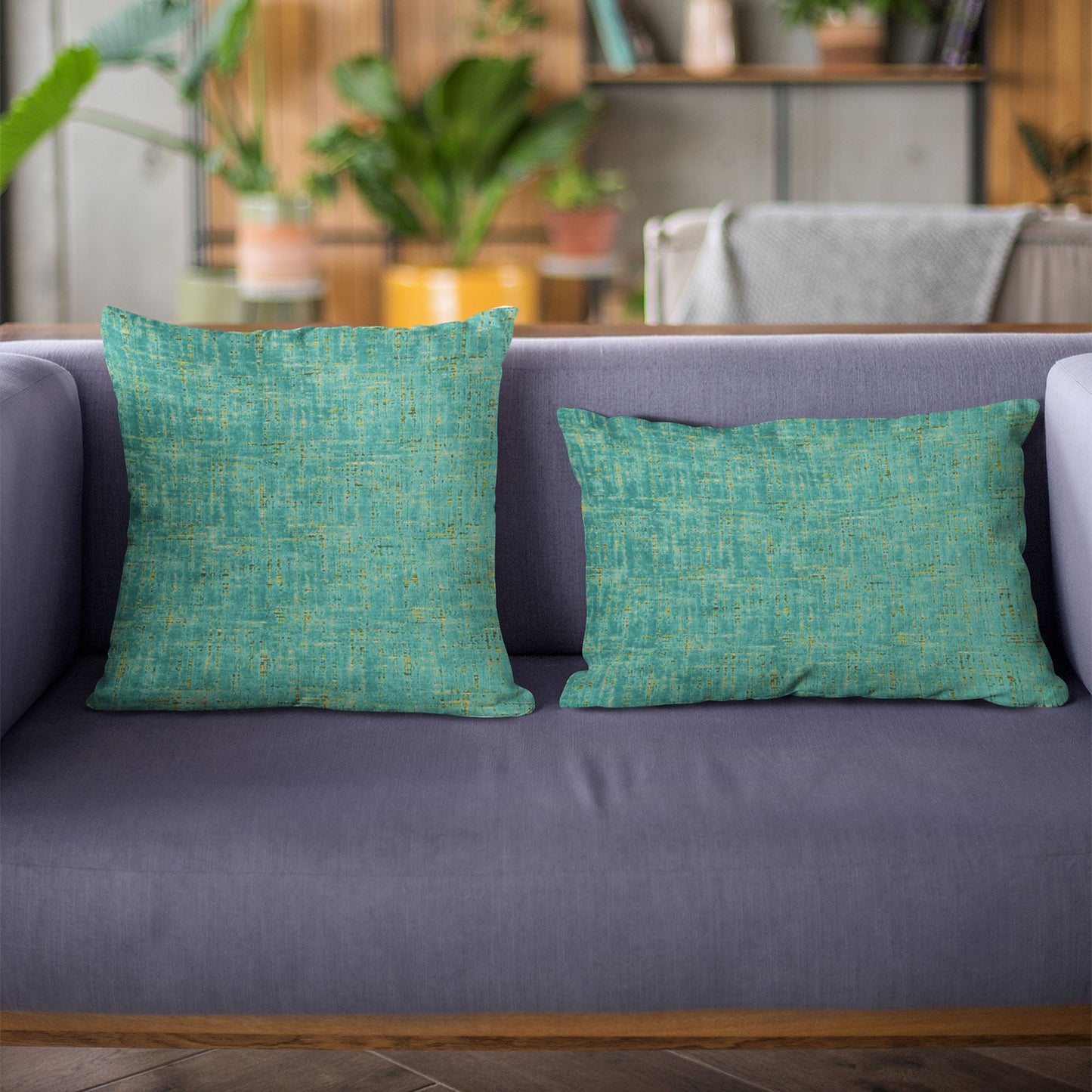 Two green textured pillows on a gray sofa with a blurred indoor background