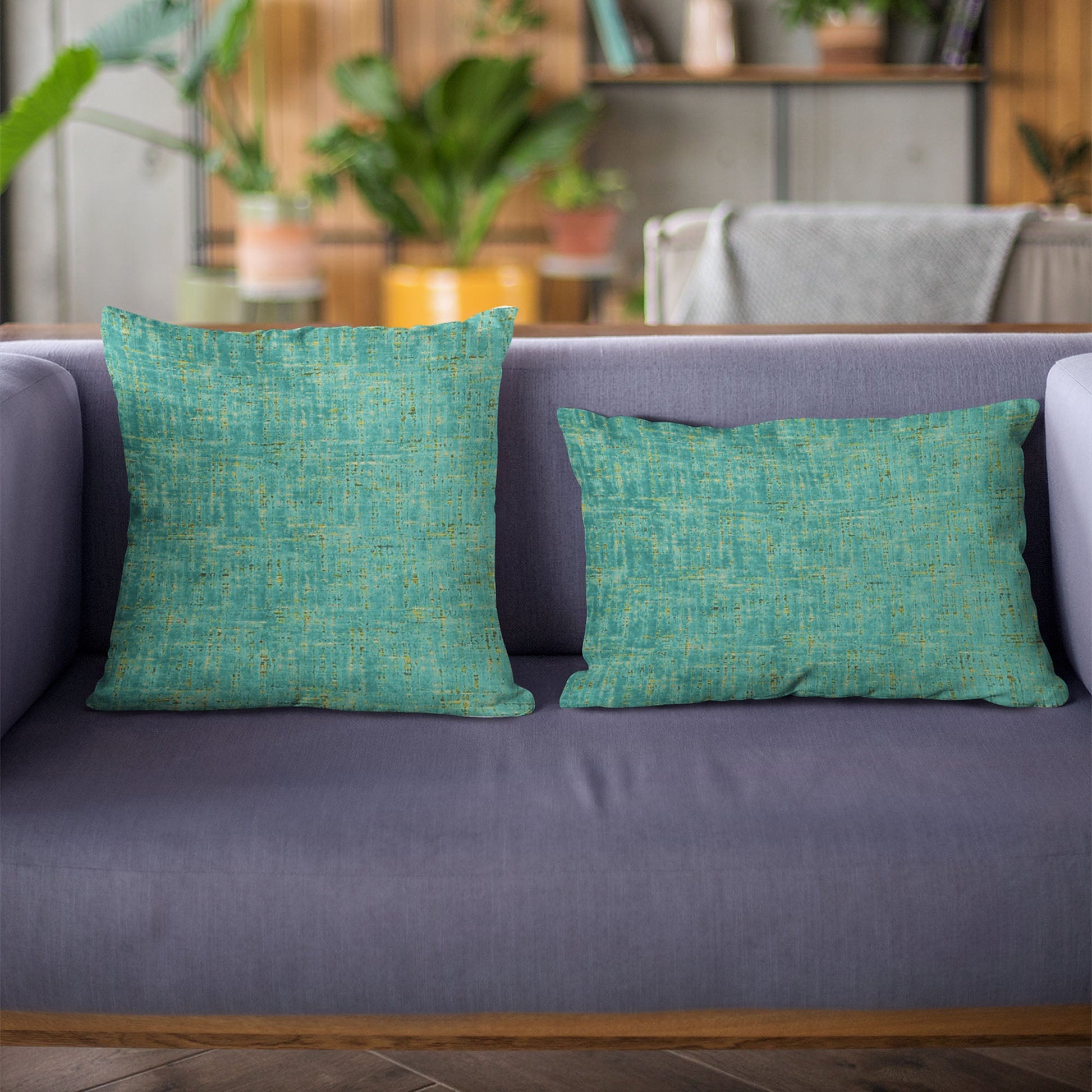 Two green textured pillows on a gray sofa with a blurred indoor background