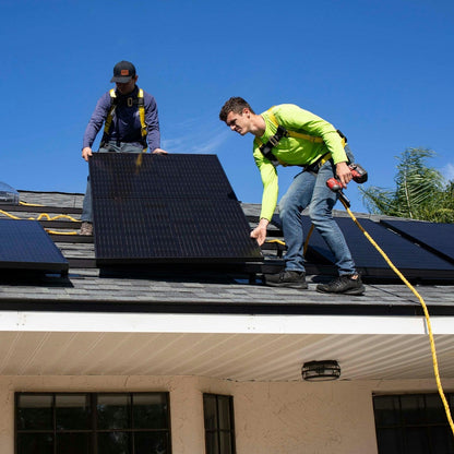 Two workers installing solar panels on a roof with a clear blue sky.