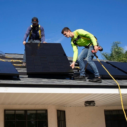 Two workers installing solar panels on a roof with a clear blue sky.