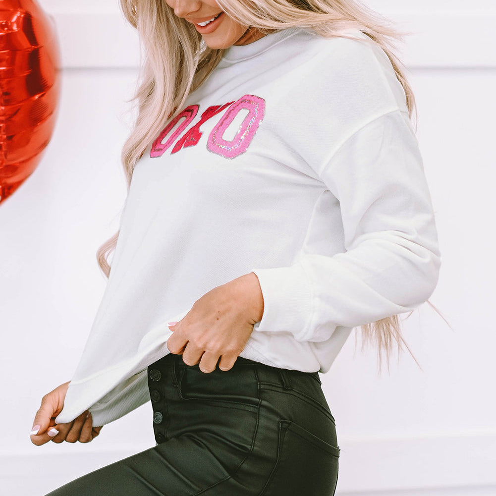 Woman wearing a white sweatshirt with pink text, standing against a white background.