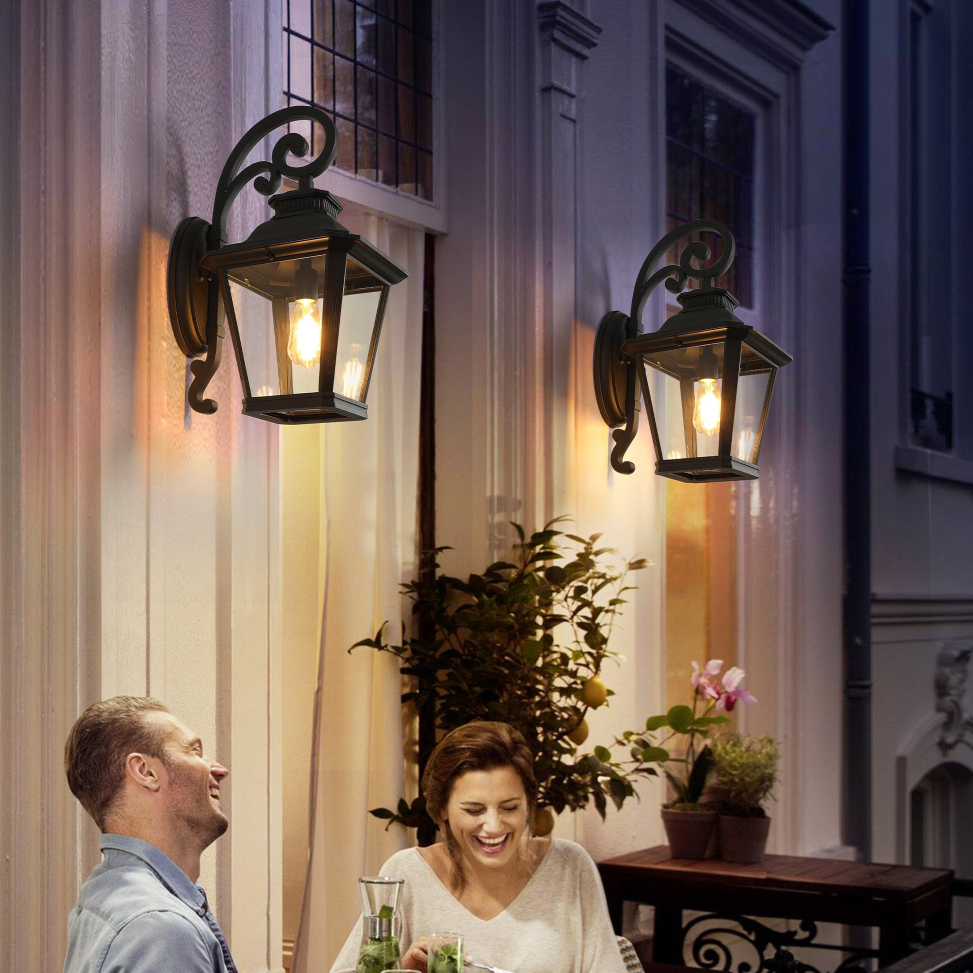Couple sitting outdoors under wall-mounted lanterns with a warm glow.