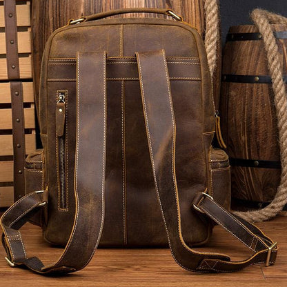 Brown leather backpack on a wooden surface with barrels and a bottle in the background