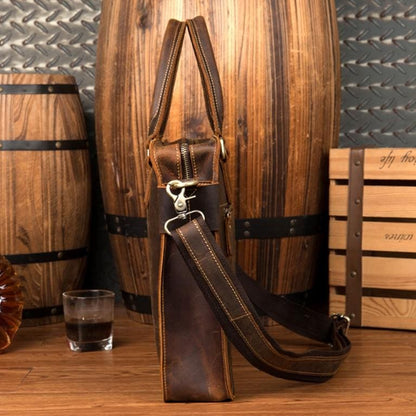 Brown leather bag with a glass of whiskey on a wooden surface with barrels in the background
