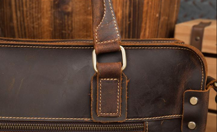 Close-up of a brown leather bag with a strap and metal buckle.